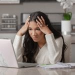 frustrated woman, hands on her head in front of laptop