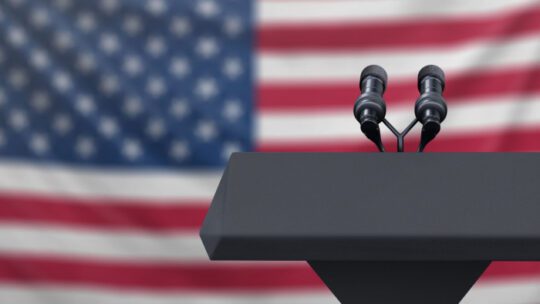 Podium lectern with two microphones and United States flag in baackground