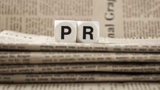 The block letters PR sitting on newspapers