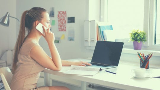 girl on phone working at laptop