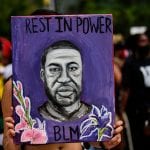 Protestor holds purple poster featuring George Floyd portrait reading "Rest in Power - BLM"