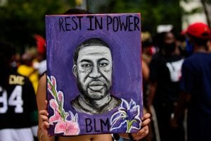 Protestor holds purple poster featuring George Floyd portrait reading "Rest in Power - BLM"