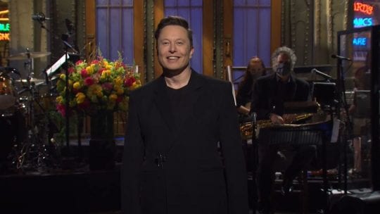 Elon Musk on SNL set, dressed in all black.