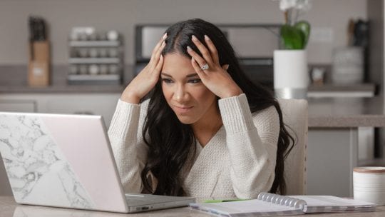 frustrated woman, hands on her head in front of laptop