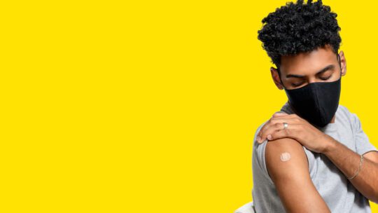 influencer showing off vaccine band-aid against yellow background