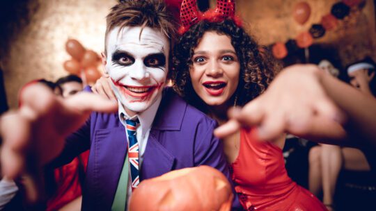 man in joker costume, woman in devil costume, smiling at camera