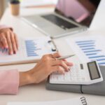 Woman using calculator with computer laptop, budgeting for PR