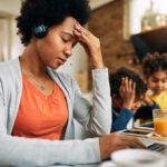 Working woman stressed out on laptop while kids play in background