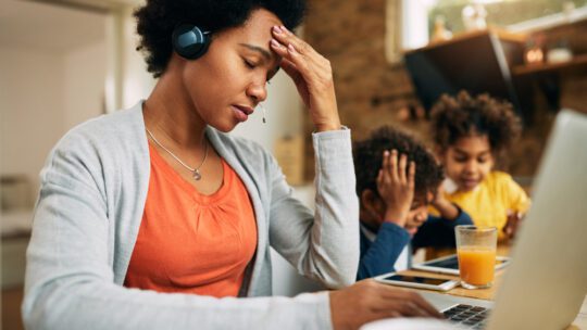 Working woman stressed out on laptop while kids play in background