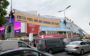 Greenpeace protestors dressed as "This is Fine" Dogs climb a fire truck to protest fossil fuel advertising at Cannes
