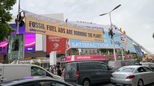 Greenpeace protestors dressed as "This is Fine" Dogs climb a fire truck to protest fossil fuel advertising at Cannes