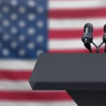 Podium lectern with two microphones and United States flag in baackground