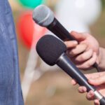 Reporter at news conference holding microphone making media interview with female politician or business woman