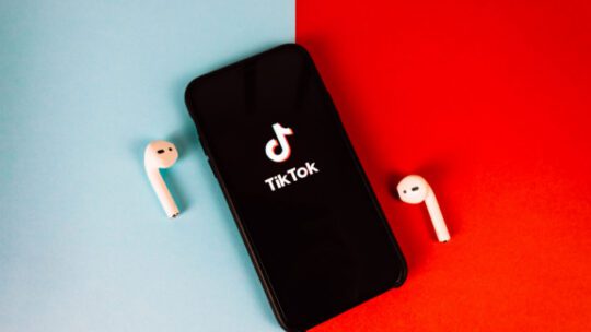 iPhone with TikTok app logo on the screen. red-blue background