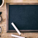 Blank blackboard with a piece of chalk, glasses and coffee on wooden background