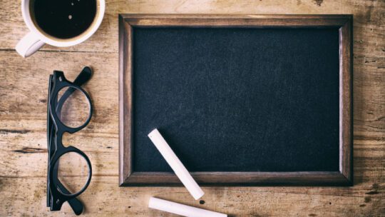 Blank blackboard with a piece of chalk, glasses and coffee on wooden background