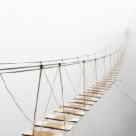 Fuzzy man walking on hanging bridge vanishing in fog.