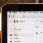 The corner of an open laptop displays a Gmail inbox on its screen. The inbox shows a list of folders on the left of the screen, with "inbox" selected