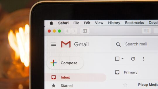 The corner of an open laptop displays a Gmail inbox on its screen. The inbox shows a list of folders on the left of the screen, with "inbox" selected