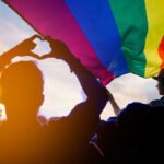 Pride community at a parade with hands raised and the LGBT flag.