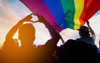 Pride community at a parade with hands raised and the LGBT flag.