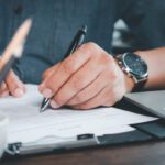 Close-up of Hand using writing pen with questionnaire or paperwork survey question filling in business company personal information form checklist document.