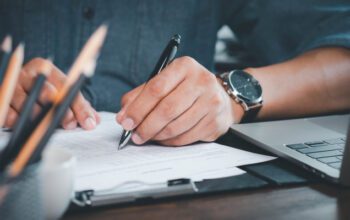 Close-up of Hand using writing pen with questionnaire or paperwork survey question filling in business company personal information form checklist document.