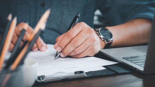 Close-up of Hand using writing pen with questionnaire or paperwork survey question filling in business company personal information form checklist document.