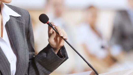 Businesswoman standing on stage and reporting for audience