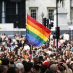 Pride community in a giant crowd with LGBT rainbow flag raised.