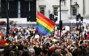 Pride community in a giant crowd with LGBT rainbow flag raised.