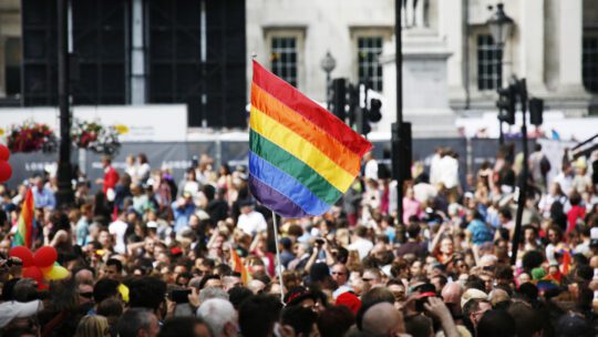 Pride community in a giant crowd with LGBT rainbow flag raised.