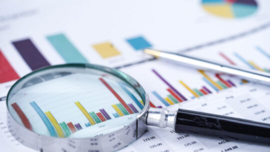 Magnifying glass on charts graphs spreadsheet paper.