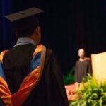 College students dressed in cap and gowns listen to a speech during a graduation ceremony.