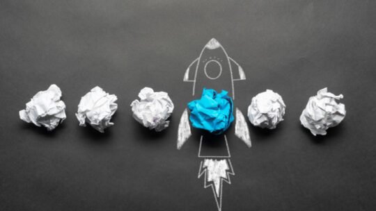 Rocket sketch drawing with crumpled blue paper ball on chalkboard.