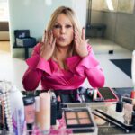 In a still from e.l.f. Cosmetics' Super Bowl commercial, Jennifer Coolidge sits elegantly at a vanity, using e.l.f. cosmetics. She applies makeup with a fun expression, enhancing her natural beauty effortlessly.