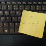 Image of a keyboard with a yellow sticky note placed on top. The sticky note has the words 'I quit' written in black ink, indicating resignation or leaving a job.