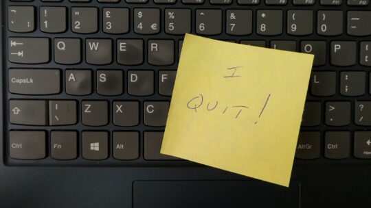 Image of a keyboard with a yellow sticky note placed on top. The sticky note has the words 'I quit' written in black ink, indicating resignation or leaving a job.