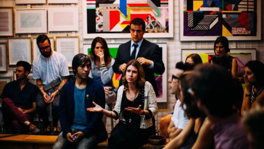 A diverse group of individuals seated in a circular arrangement, engaged in a lively and animated conversation, reflecting active communication and collaboration.