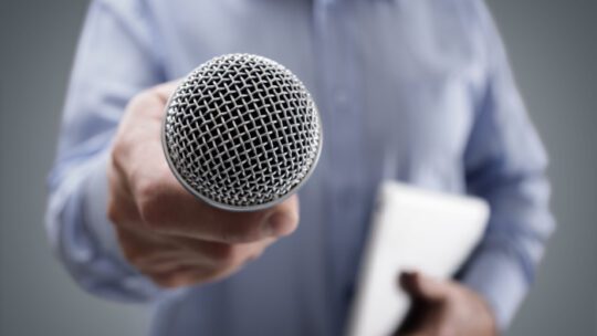 Hand holding a microphone conducting a business interview or press conference