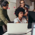 women in an office talking, working and looking at a computer screen