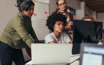 women in an office talking, working and looking at a computer screen