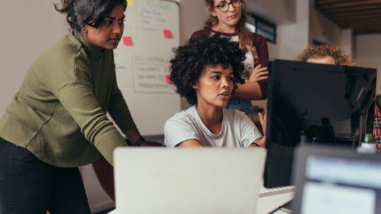 women in an office talking, working and looking at a computer screen