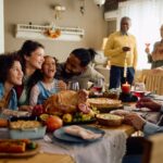Happy multiracial parents and their kids laughing during family meal on Thanksgiving in dining room.