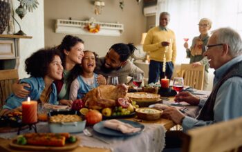 Happy multiracial parents and their kids laughing during family meal on Thanksgiving in dining room.