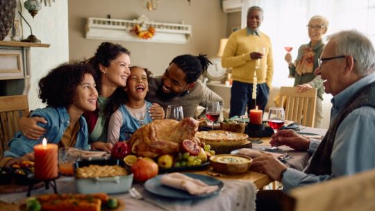 Happy multiracial parents and their kids laughing during family meal on Thanksgiving in dining room.