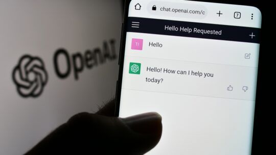 Person holding cellphone with webpage of US artificial intelligence company OpenAI LLC on screen with logo. Focus on center of phone display.