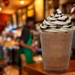 Cup of iced medium coffee or Frappuccino with cream and chocolate sauce on wooden counter at cafe or coffee shop.