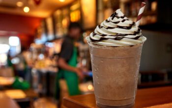 Cup of iced medium coffee or Frappuccino with cream and chocolate sauce on wooden counter at cafe or coffee shop.