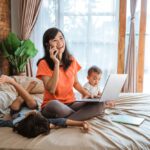 young woman working on her bed while taking care of her unruly children at home